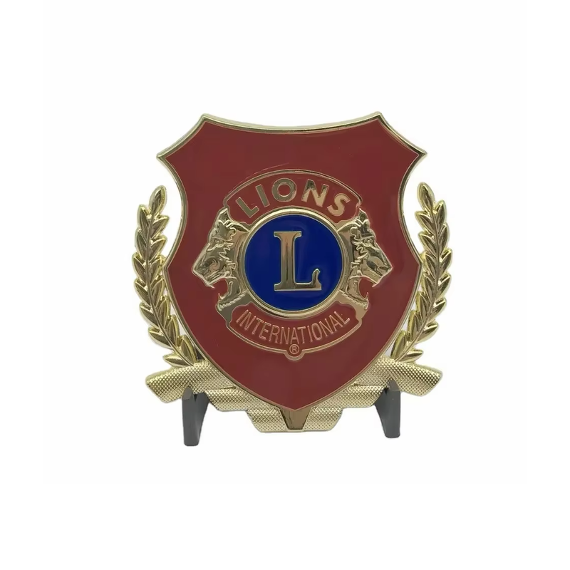 Red shield-shaped display plaque with gold-tone laurel branches, a blue central L emblem and Lions International lettering, supported by a black stand on white.
