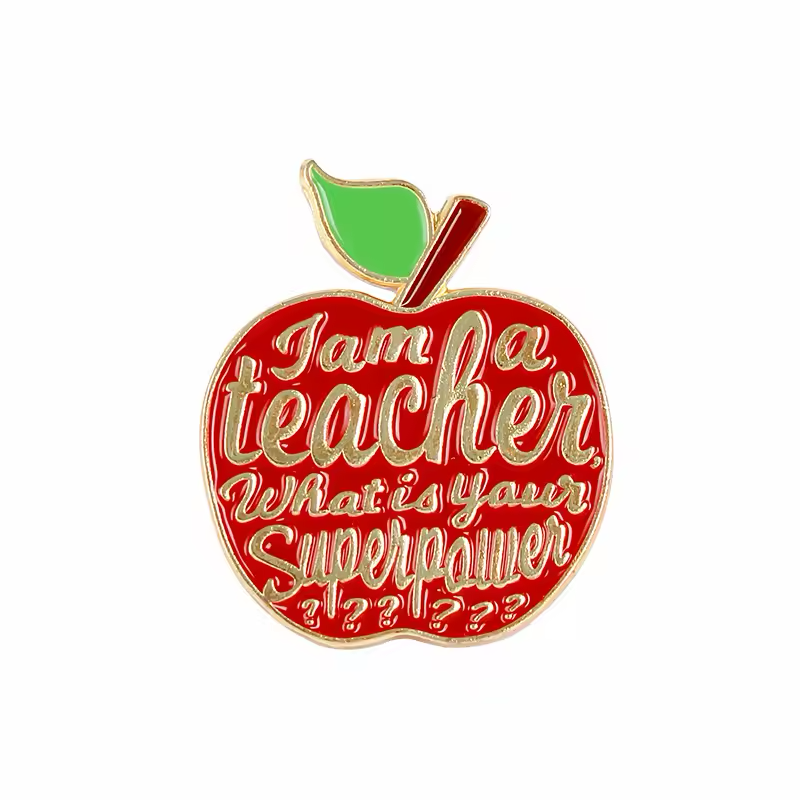 Red apple-shaped teacher pin with a green leaf, gold-tone outlines and lettering reading I am a teacher, What is your Superpower on a white background.