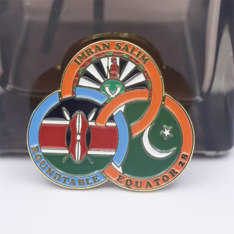 Three interlocking ring emblem pin with Kenya and Pakistan flag elements, orange and blue borders, gold-tone outlines, and IMRAN SALIM, ROUNDTABLE and EQUATOR 28 lettering against a dark display background.