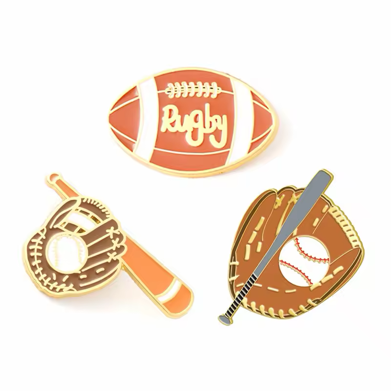 Three gold-tone sports pins showing a rugby ball and two baseball glove, ball and bat designs.