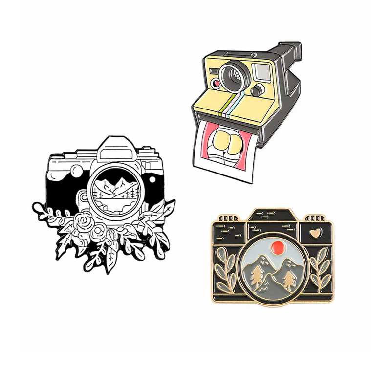 Three camera pins featuring a yellow instant camera, a floral black-and-white camera and a black camera with a mountain scene.