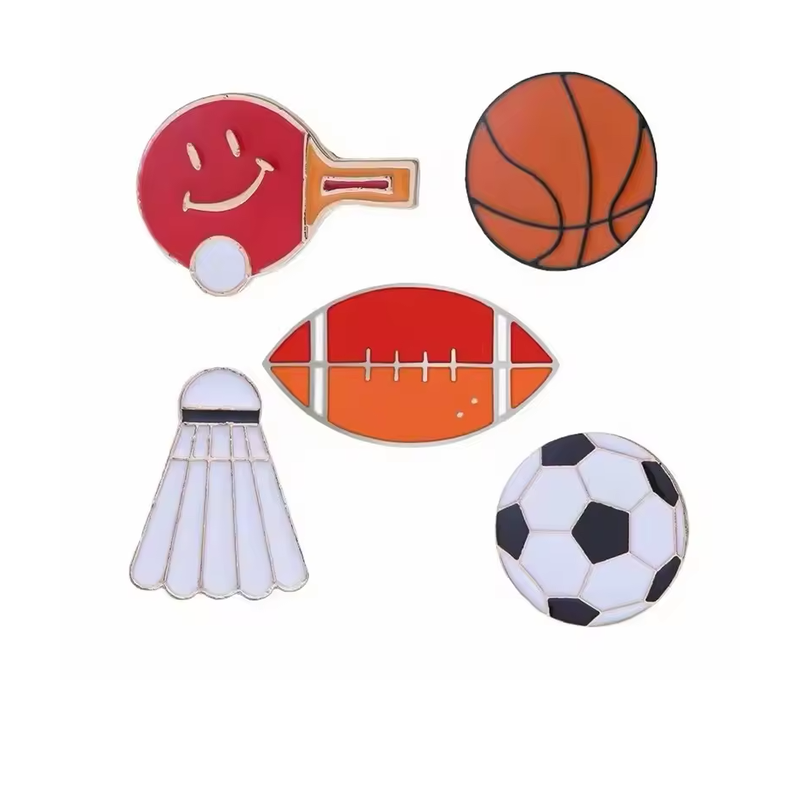 Sports pins showing a smiling red table tennis paddle with a white ball, an orange basketball, a red-orange football, a white shuttlecock and a black and white soccer ball.