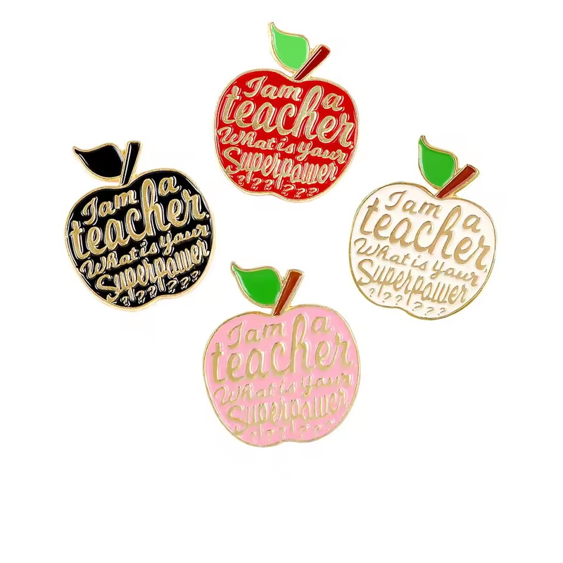 Four apple-shaped teacher pins in red, black, white and pink, with gold-tone lettering reading I am a teacher, What is your Superpower on a white background.
