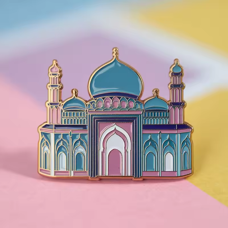 Mosque-shaped pin with teal domes, pink and purple architectural details, two minarets, arched openings and gold-tone outlines on a pastel multicolor background.