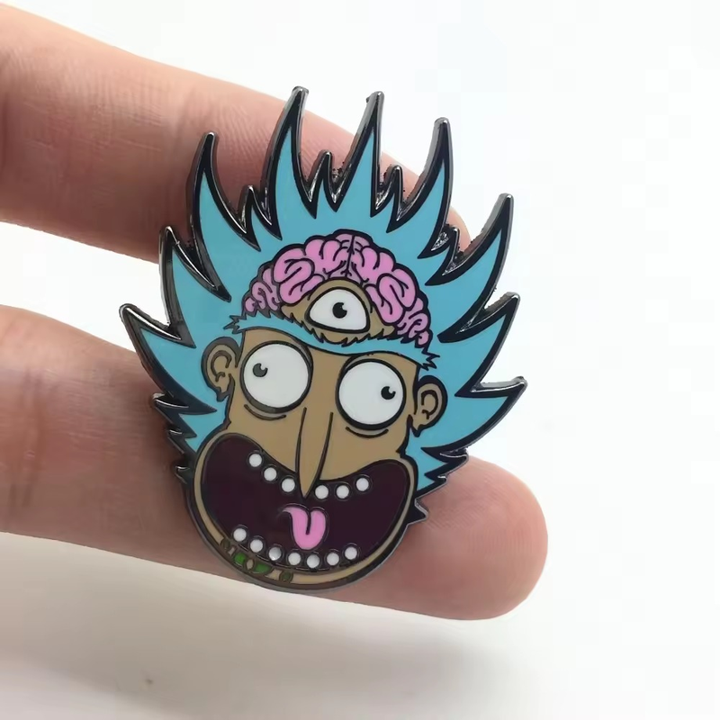 Hand holding a blue-haired, three-eyed cartoon face pin with a pink brain detail and an open mouth.
