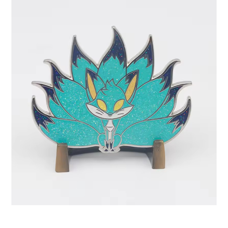 Turquoise glitter fox pin with fanned tails, yellow eyes and dark blue tips, displayed on a wooden stand.