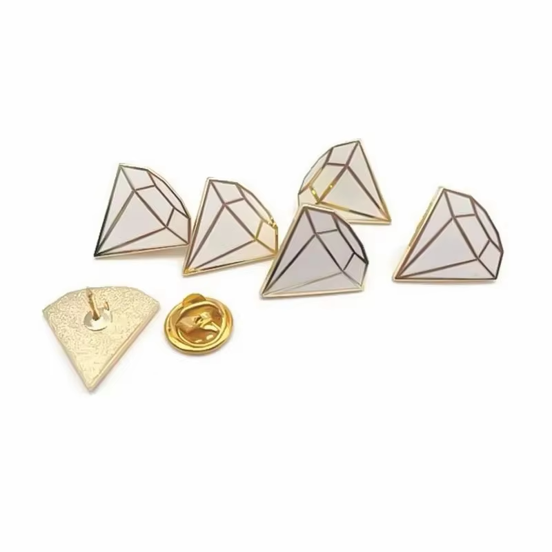 Five white faceted diamond-shaped pins with dark or gold-tone outlines, beside a reverse view with a pin post and a gold-tone butterfly clutch on white.
