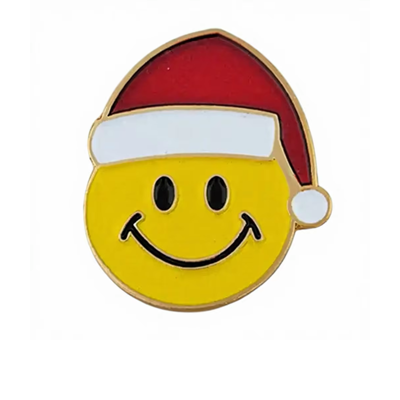 Yellow smiley face pin wearing a red Santa hat with white trim and a white pompom, black oval eyes and gold-tone outlines on a white background.