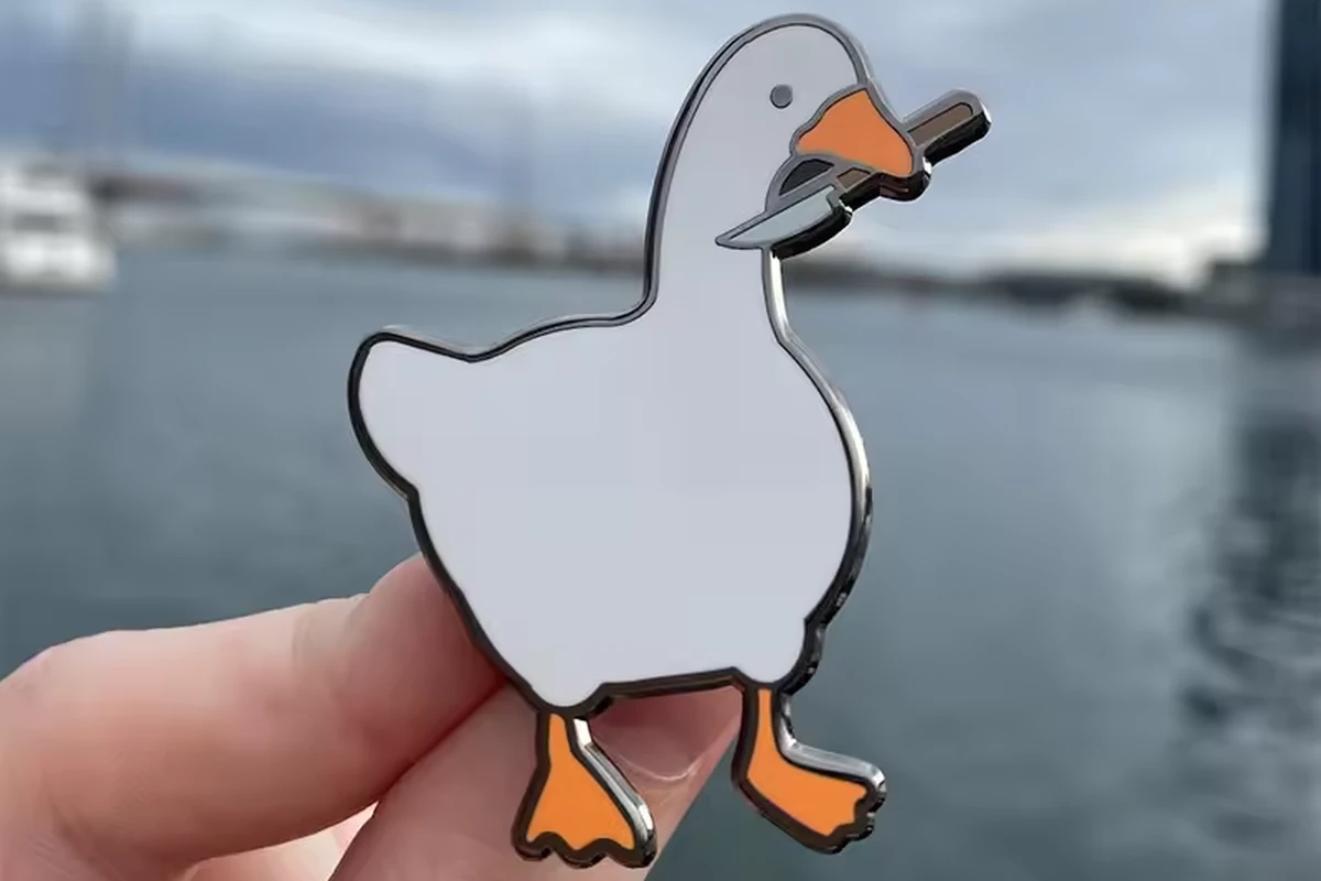 A hand holding a white goose pin outdoors.