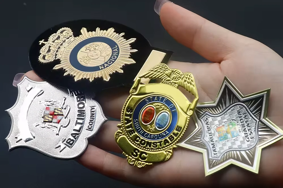 A hand holding several professional insignia badges in gold and silver finishes.
