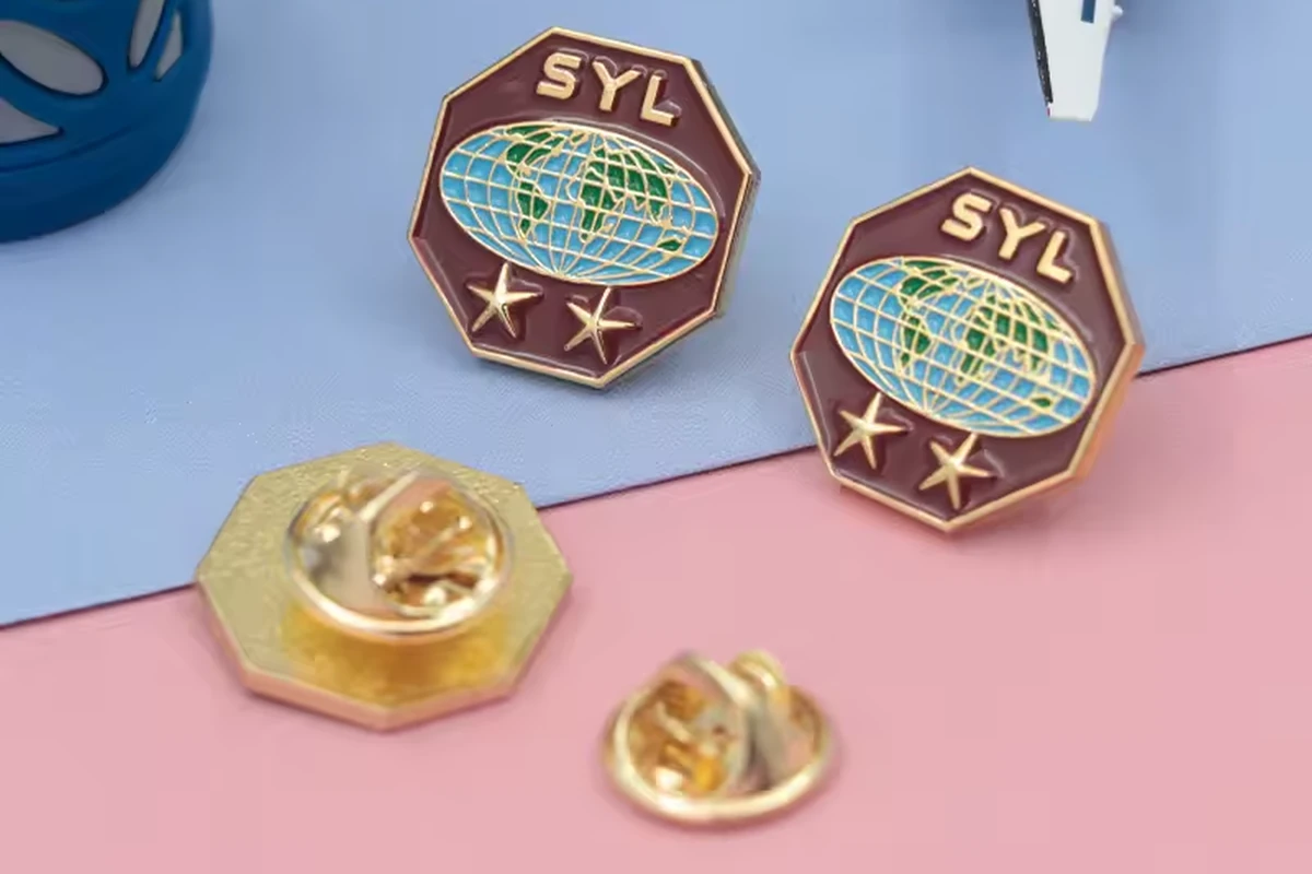 Two globe-design enamel pins with gold butterfly clutches on a blue and pink surface.