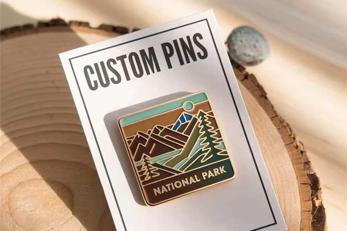 Mountain-themed enamel pin on a white backing card placed on a wood slice.