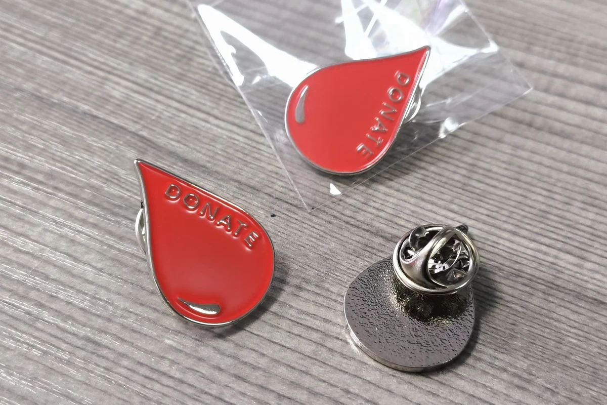 Red drop-shaped pins on a wood surface, with one pin in a clear bag and another shown from the back with its clutch.