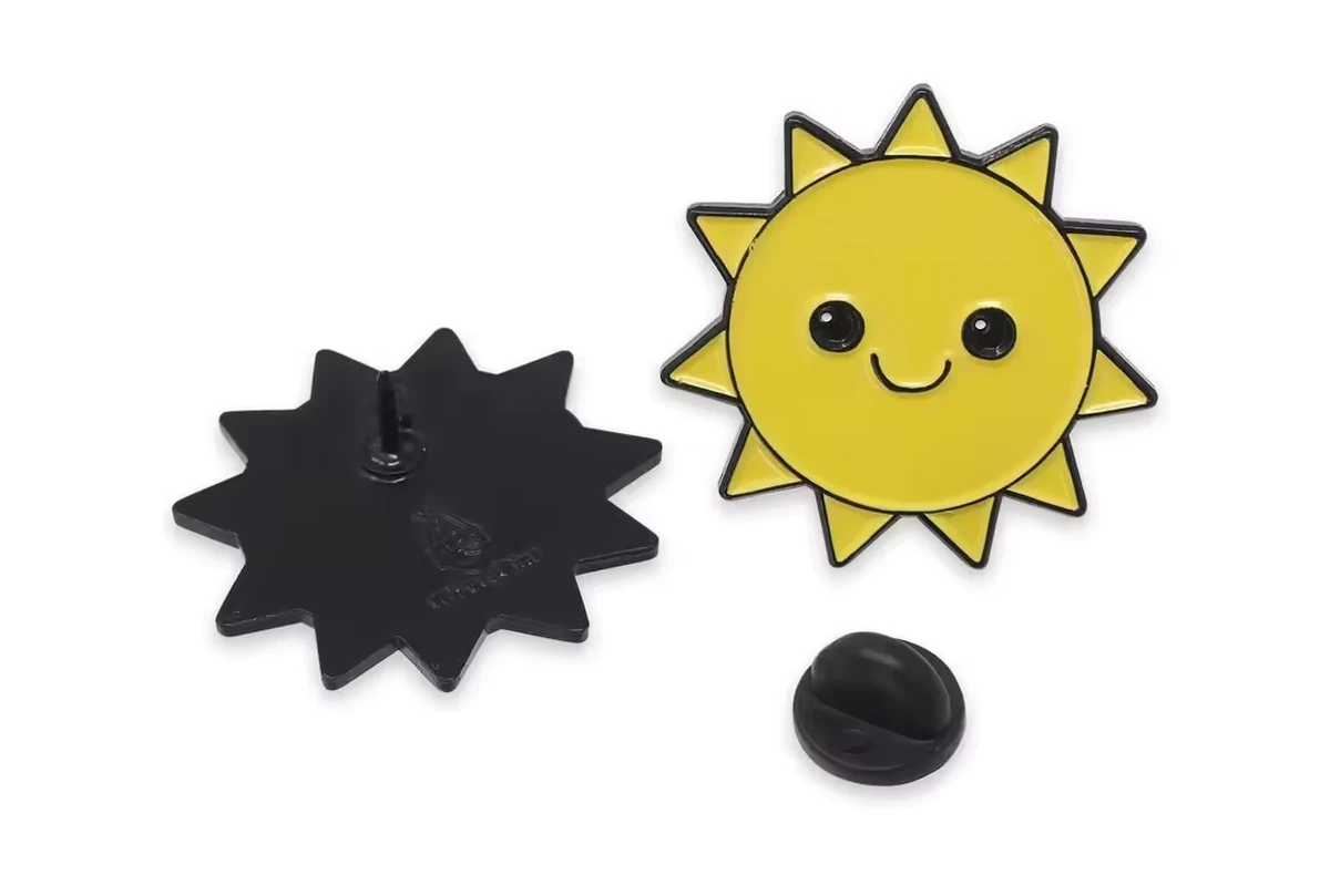 A smiling yellow sun pin with its dark reverse and a separate black rubber clutch.