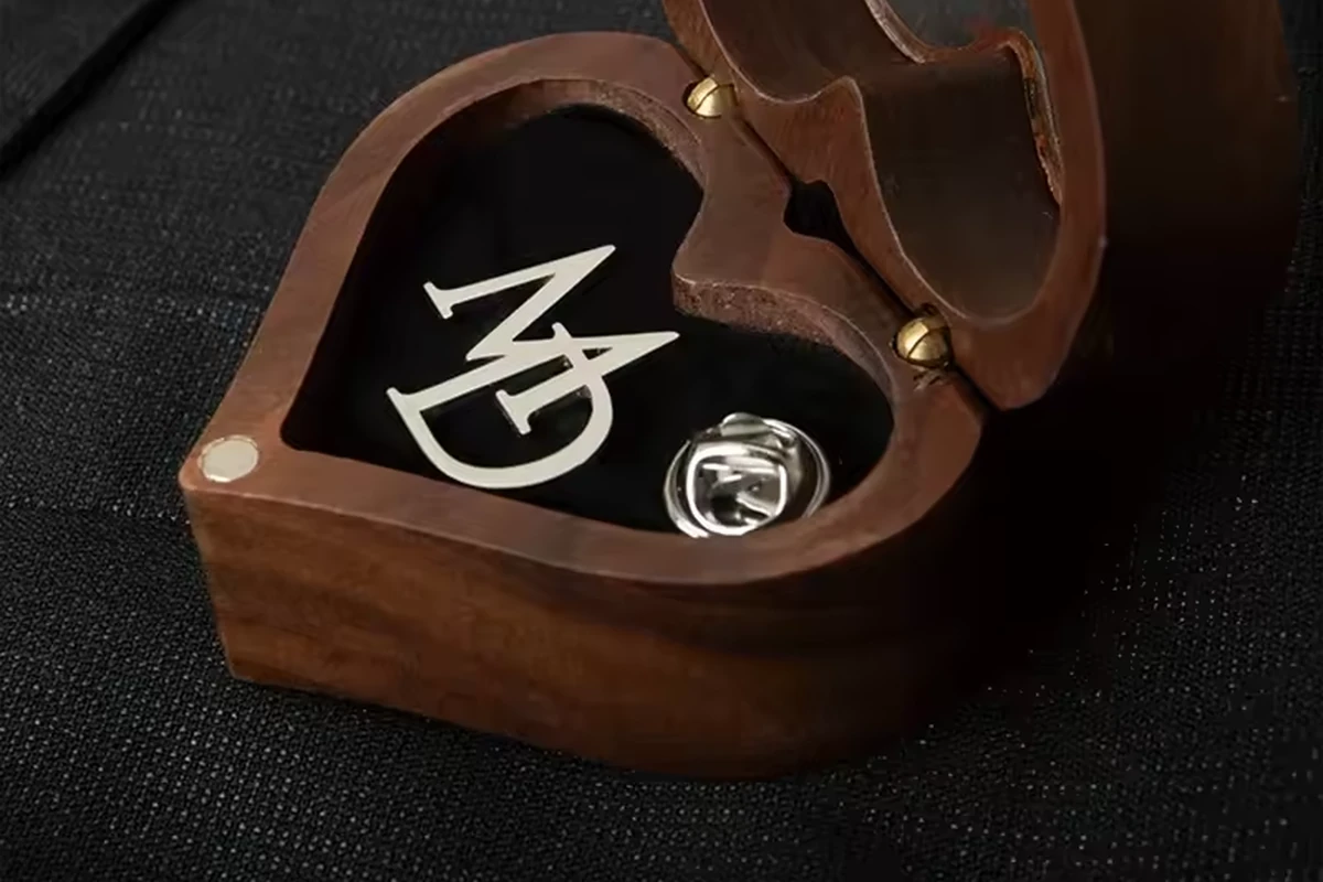 A close view of a logo pin and metal butterfly clutch inside a wooden presentation box.